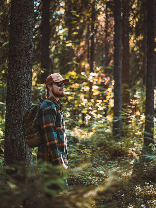 Man i rutig overshirt och keps med ryggsäck i skogen