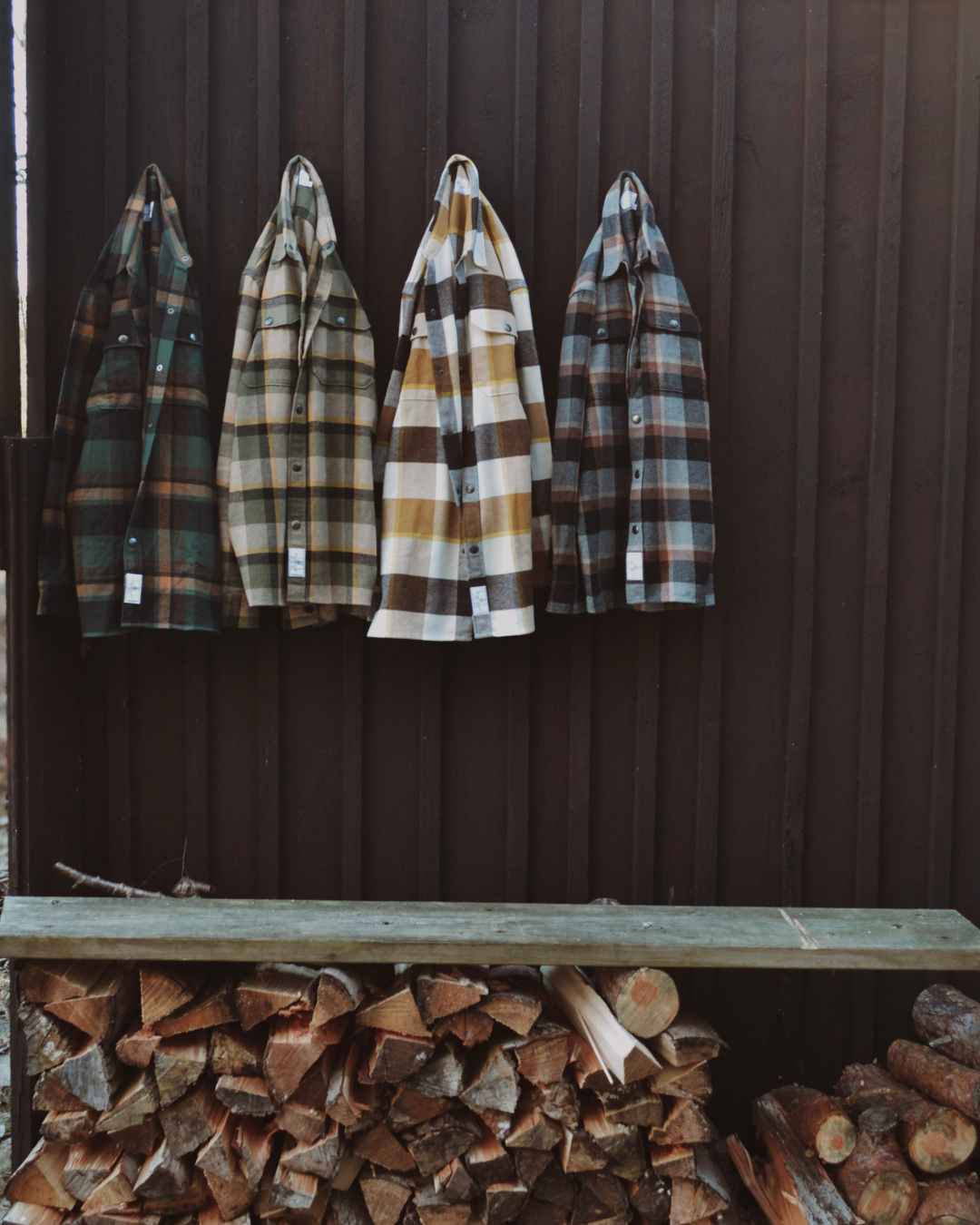 Fyra flanell-overshirts i olika färger och rutigmönster hängda på en trävägg.