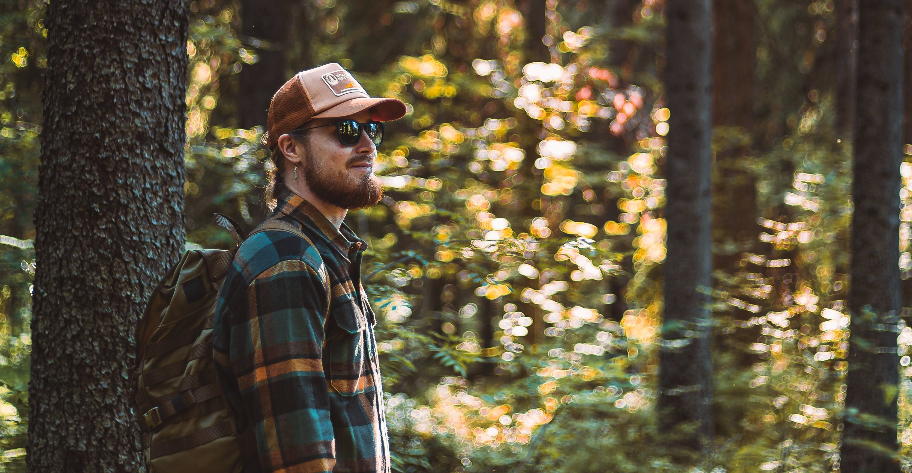 Man i rutig overshirt och keps med ryggsäck i skogen