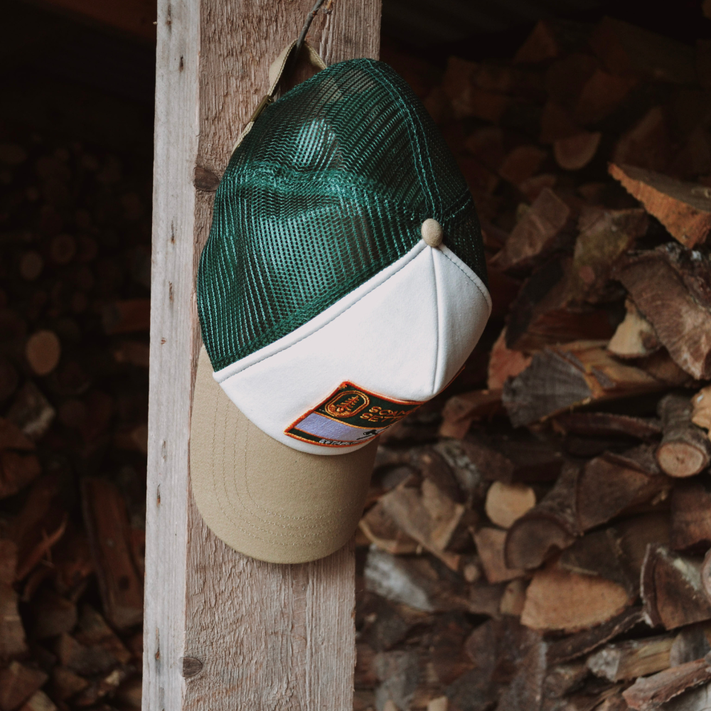 Grön truckerkeps i outdoorstil placerad på vedbod